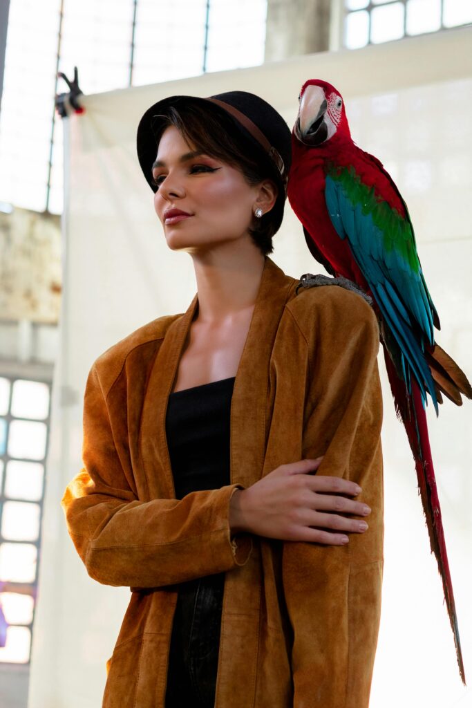 Fashionable woman posing with a vibrant macaw perched on her shoulder.
