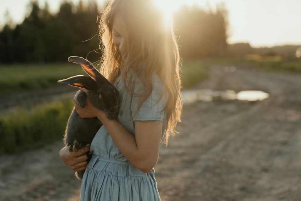 pexels-photo-4921291-4921291 A young girl lovingly holds a rabbit outdoors at sunset, surrounded by picturesque farmland.